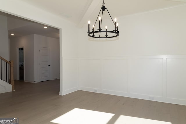 unfurnished dining area featuring beamed ceiling, light wood-type flooring, ornamental molding, and an inviting chandelier