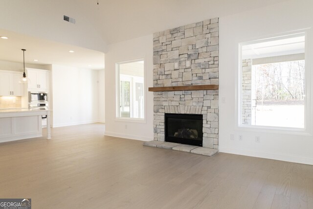 unfurnished living room featuring plenty of natural light, a stone fireplace, and light hardwood / wood-style flooring