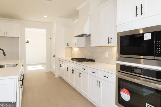 kitchen featuring white cabinets, sink, light hardwood / wood-style flooring, decorative backsplash, and stainless steel appliances