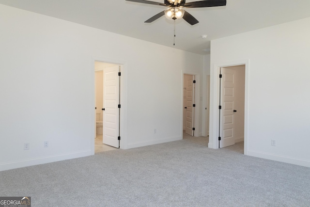 unfurnished bedroom with ensuite bath, ceiling fan, light colored carpet, and a walk in closet