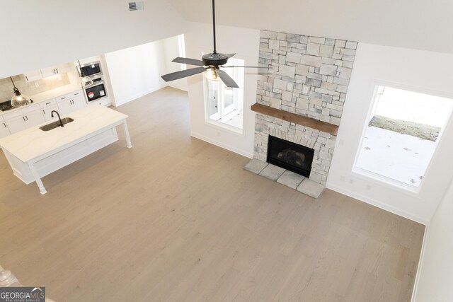 unfurnished living room featuring high vaulted ceiling, sink, light hardwood / wood-style flooring, ceiling fan, and a fireplace