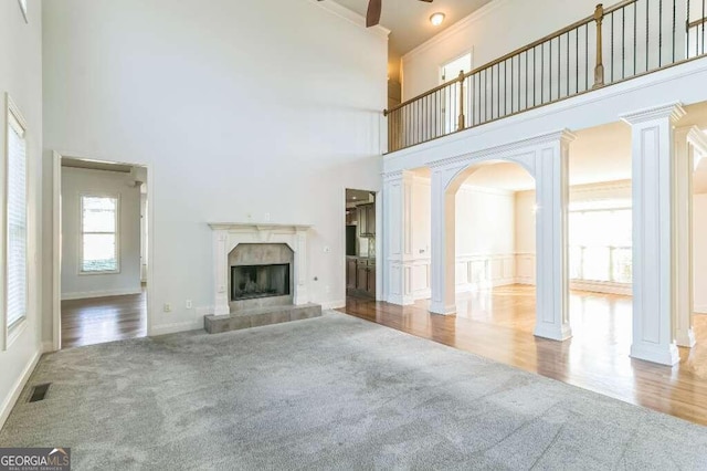 unfurnished living room featuring a towering ceiling, a tiled fireplace, wood-type flooring, and decorative columns