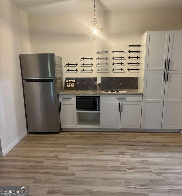 kitchen with light hardwood / wood-style floors, white cabinets, light stone countertops, and stainless steel refrigerator