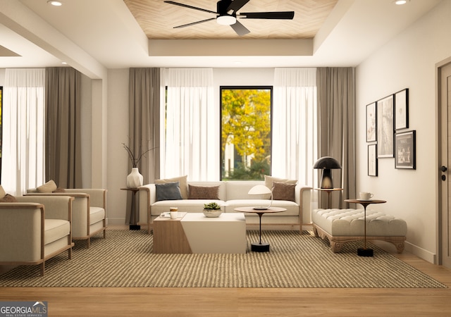 living area with light hardwood / wood-style flooring, a tray ceiling, and ceiling fan