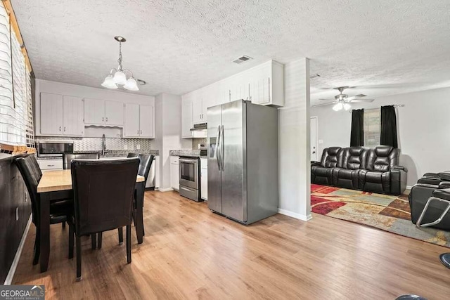 kitchen with pendant lighting, light wood-type flooring, appliances with stainless steel finishes, a textured ceiling, and ceiling fan with notable chandelier