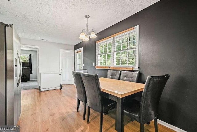 dining space with a textured ceiling, light hardwood / wood-style flooring, and a chandelier