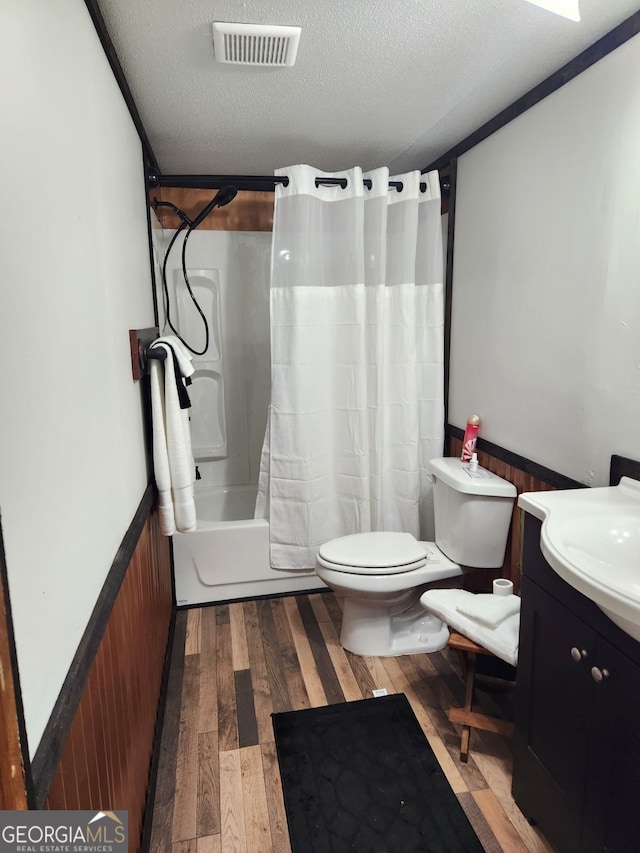 full bathroom featuring vanity, a textured ceiling, shower / bath combo with shower curtain, wood-type flooring, and toilet