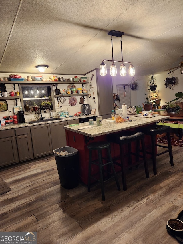 bar with sink, hanging light fixtures, light stone countertops, a textured ceiling, and wood-type flooring