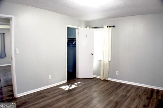 unfurnished bedroom featuring dark wood-type flooring, a textured ceiling, a walk in closet, and a closet