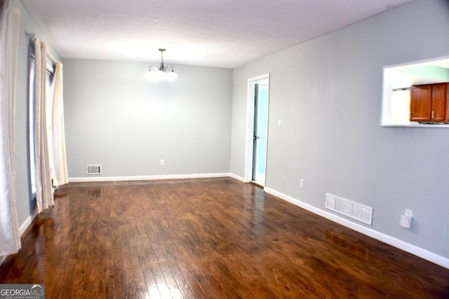 spare room featuring a notable chandelier and dark hardwood / wood-style floors