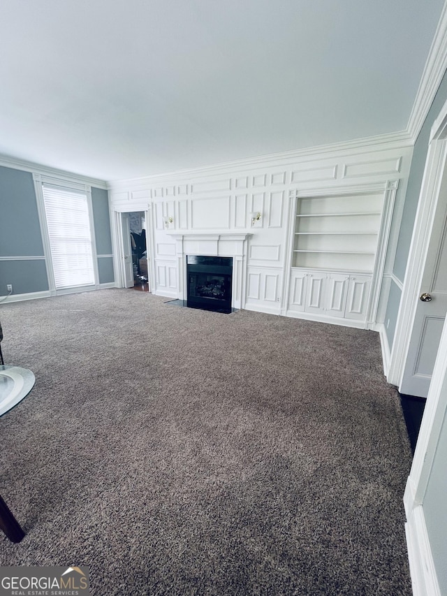 unfurnished living room featuring dark colored carpet, crown molding, and built in shelves