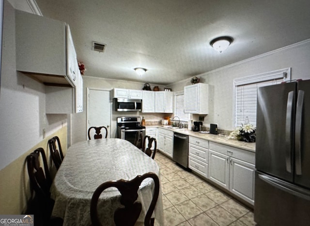 kitchen with stainless steel appliances, ornamental molding, sink, light tile patterned floors, and white cabinets