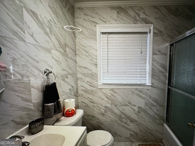 full bathroom featuring vanity, toilet, combined bath / shower with glass door, and tile walls