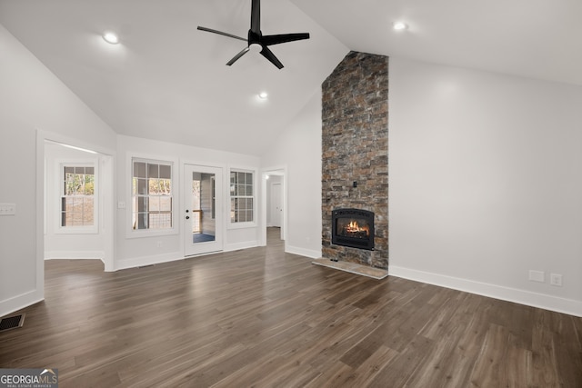 unfurnished living room with dark wood-type flooring, ceiling fan, a stone fireplace, and high vaulted ceiling