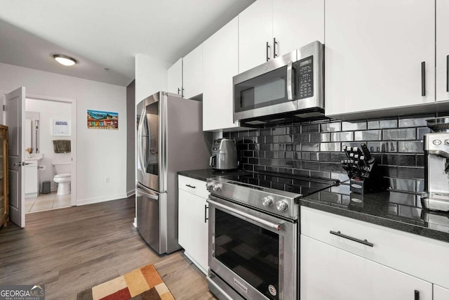 kitchen featuring appliances with stainless steel finishes, tasteful backsplash, light hardwood / wood-style flooring, dark stone countertops, and white cabinetry