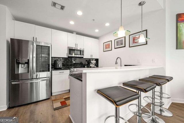 kitchen with kitchen peninsula, dark hardwood / wood-style floors, decorative light fixtures, white cabinetry, and stainless steel appliances