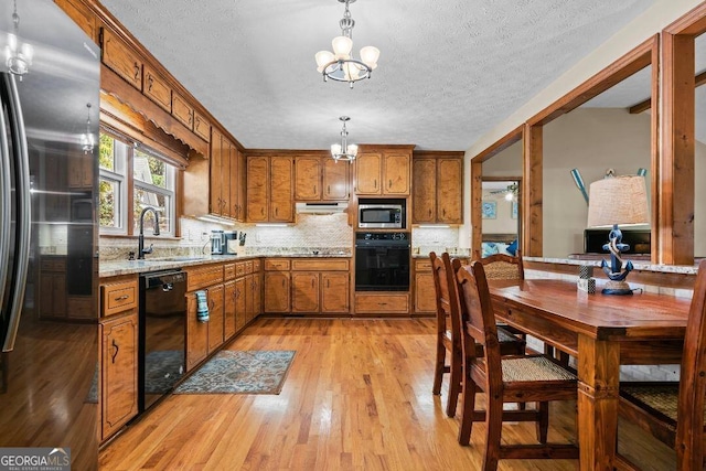 kitchen with an inviting chandelier, light wood-type flooring, black appliances, sink, and decorative light fixtures