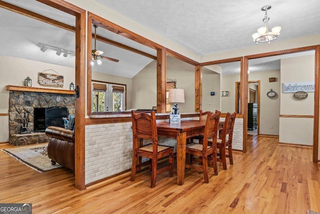 dining space featuring lofted ceiling, rail lighting, a textured ceiling, light wood-type flooring, and a fireplace