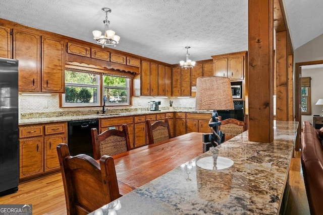 kitchen with hanging light fixtures, black appliances, sink, a notable chandelier, and light wood-type flooring