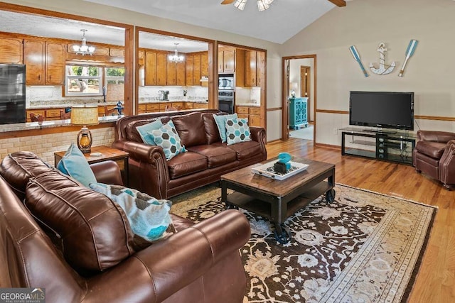 living room featuring lofted ceiling, light wood-type flooring, and ceiling fan with notable chandelier