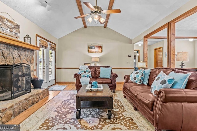 living room featuring vaulted ceiling with beams, a stone fireplace, light wood-type flooring, and ceiling fan