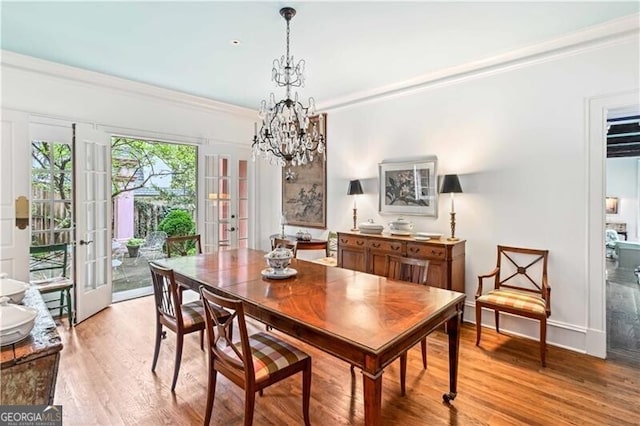 dining area with a chandelier, light wood-type flooring, crown molding, and french doors