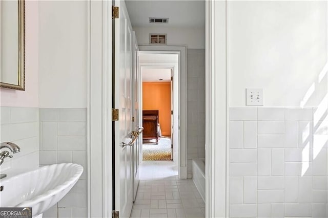 bathroom with a washtub, sink, and tile walls