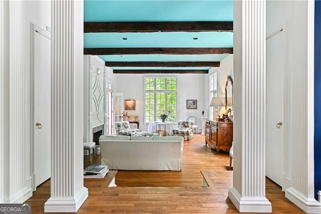 living room featuring beamed ceiling, light wood-type flooring, and decorative columns