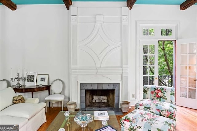 living room featuring wood-type flooring, beam ceiling, and a tiled fireplace