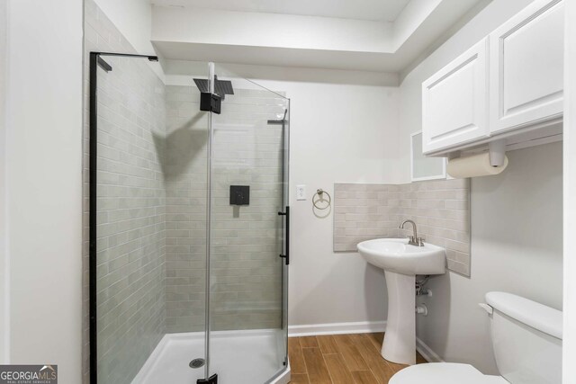 bathroom featuring wood-type flooring, sink, backsplash, a shower with shower door, and toilet