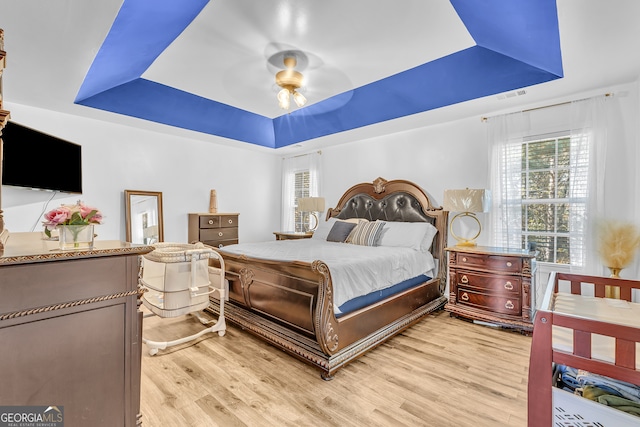 bedroom featuring light wood-type flooring, a raised ceiling, and ceiling fan