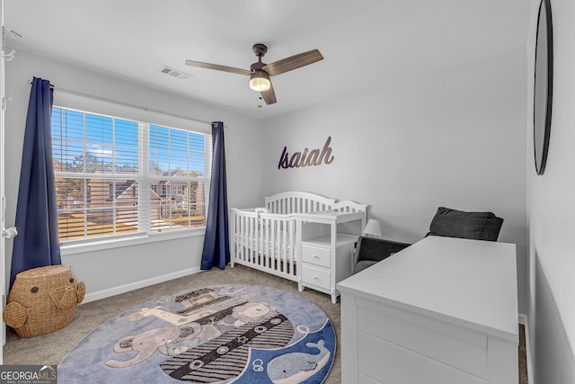 carpeted bedroom with a crib and ceiling fan