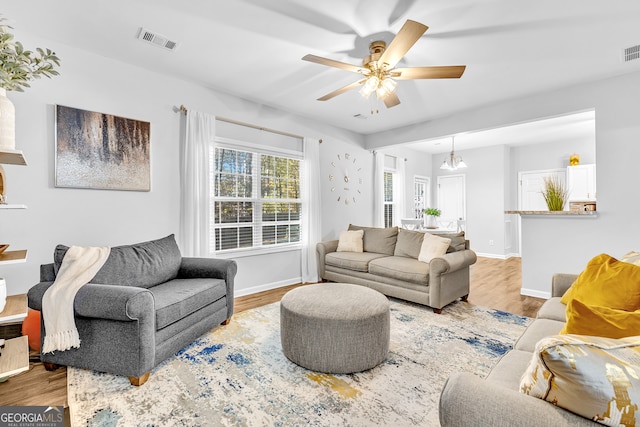 living room with ceiling fan with notable chandelier and light wood-type flooring