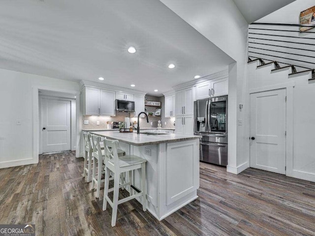 kitchen with dark hardwood / wood-style flooring, an island with sink, white cabinetry, sink, and stainless steel appliances