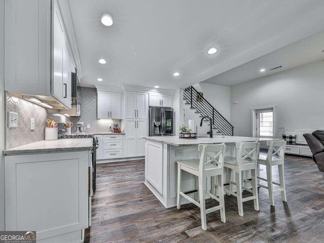 kitchen featuring a kitchen island with sink, electric range, stainless steel fridge with ice dispenser, white cabinets, and dark hardwood / wood-style flooring