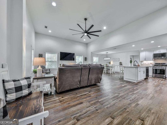 living room featuring sink, a high ceiling, dark hardwood / wood-style floors, and ceiling fan with notable chandelier