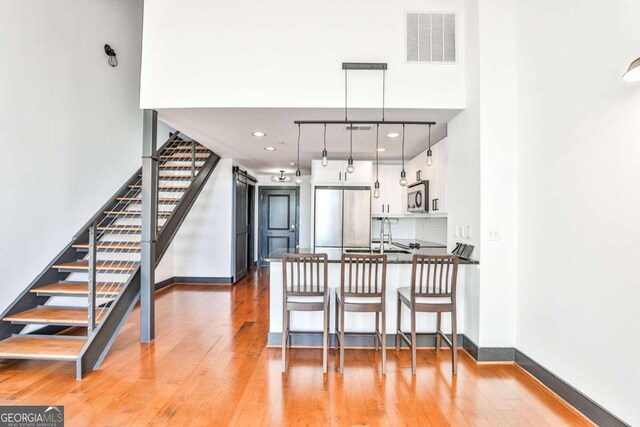 kitchen featuring appliances with stainless steel finishes, light wood-type flooring, a kitchen bar, white cabinetry, and decorative light fixtures