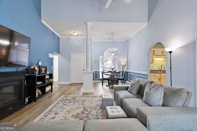 living room featuring crown molding, sink, light hardwood / wood-style floors, a high ceiling, and ceiling fan with notable chandelier