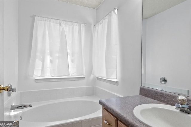 bathroom featuring vanity, a textured ceiling, and a relaxing tiled tub