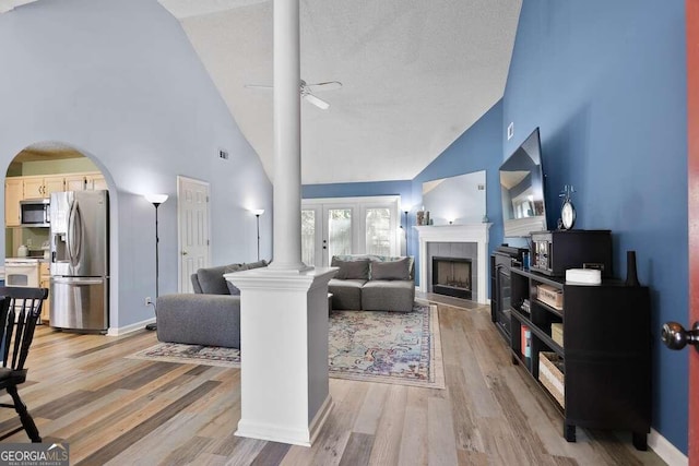 living room with a textured ceiling, high vaulted ceiling, ceiling fan, a fireplace, and light wood-type flooring