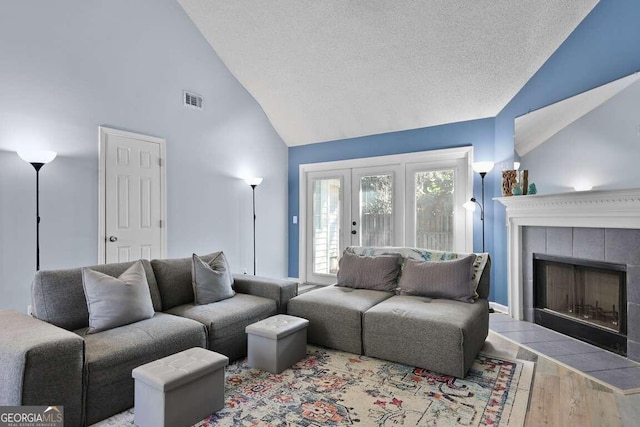 living room with a tiled fireplace, high vaulted ceiling, light hardwood / wood-style floors, and a textured ceiling