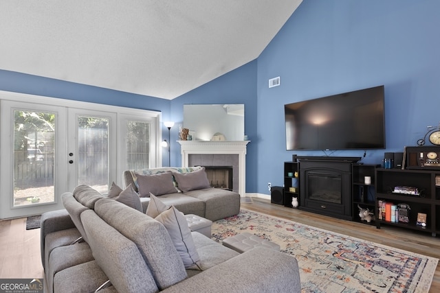 living room featuring high vaulted ceiling, a wealth of natural light, a tile fireplace, and light hardwood / wood-style floors