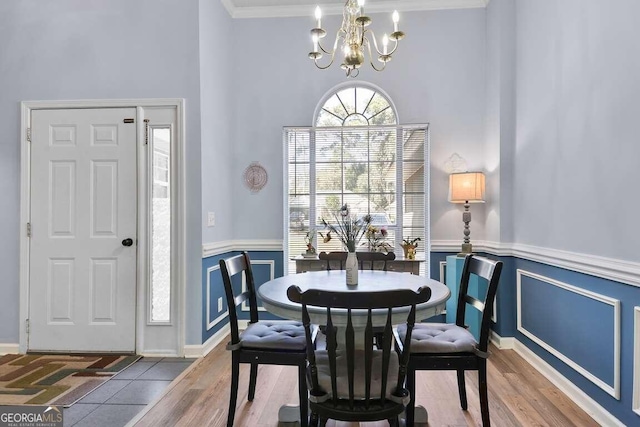 dining space with hardwood / wood-style flooring, a high ceiling, an inviting chandelier, and ornamental molding