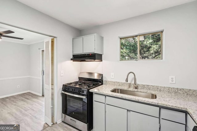 kitchen featuring sink, light wood-type flooring, stainless steel range with gas stovetop, ceiling fan, and light stone counters