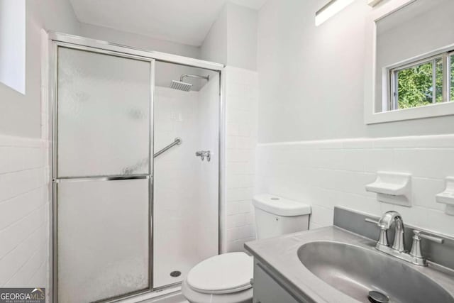 bathroom with a shower with door, tile walls, vanity, and toilet