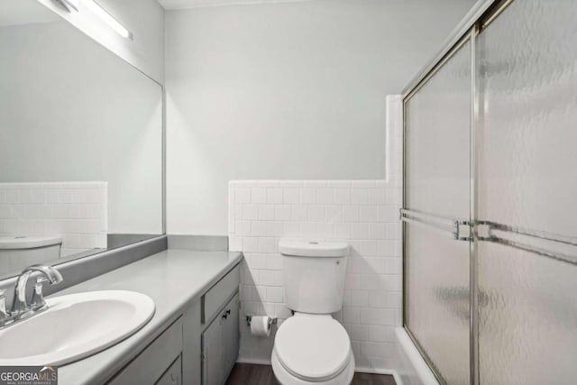 bathroom with toilet, an enclosed shower, vanity, and tile walls