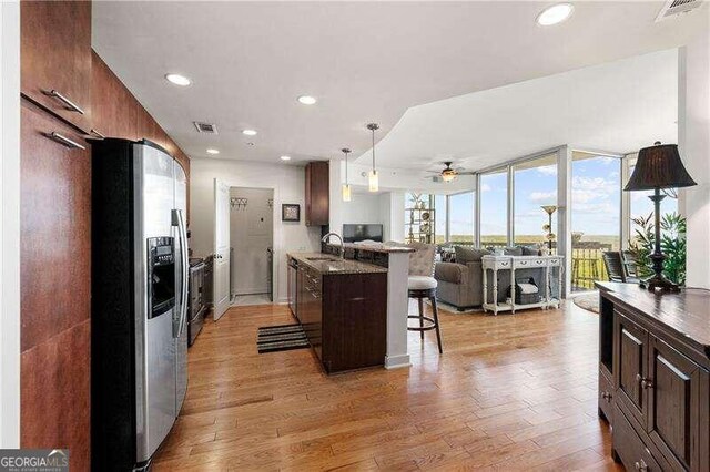 kitchen featuring a breakfast bar, stainless steel fridge with ice dispenser, decorative light fixtures, light hardwood / wood-style floors, and ceiling fan