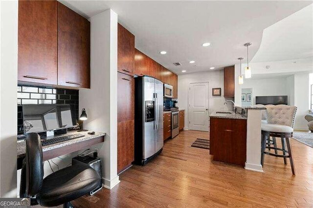 kitchen with a breakfast bar area, light hardwood / wood-style flooring, kitchen peninsula, sink, and appliances with stainless steel finishes