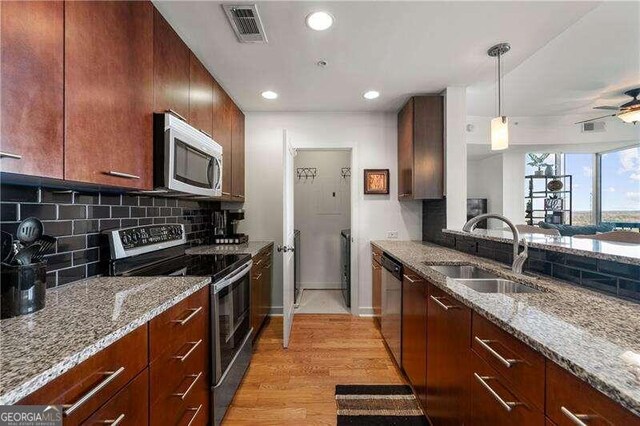 kitchen with light stone countertops, appliances with stainless steel finishes, sink, backsplash, and light hardwood / wood-style floors