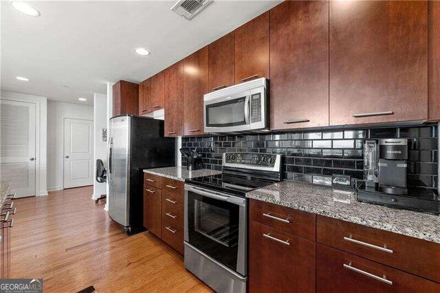 kitchen with light hardwood / wood-style flooring, light stone countertops, stainless steel appliances, and backsplash